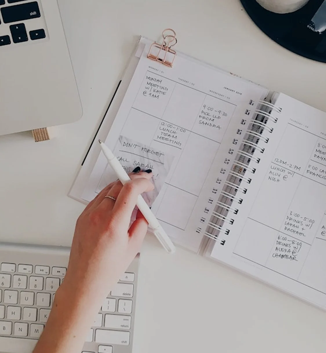 A hand checking items off a paper planner next to a keyboard